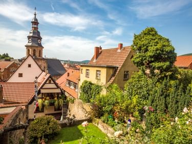 View of Kulmbach old town with traditional houses, red-tiled roofs, a prominent church tower, and a green garden courtyard under blue sky.