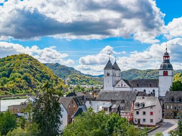 Panoramablick auf Treis-Karden mit historischen Kirchtürmen über traditionellen Häusern, umgeben von grünen Hügeln und der Mosel.