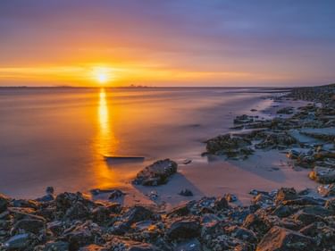 Goldener Sonnenuntergang über der Nordsee bei Emden mit felsiger Küste im Vordergrund und Schiffen am Horizont.