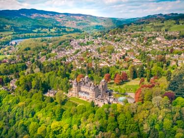 Luftaufnahme von Pitlochry in den grünen schottischen Highlands mit dem historischen Atholl Palace Hotel umgeben von Wäldern und Hügeln.