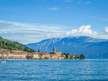 Blick auf die Stadt Salò am Gardasee mit historischen Gebäuden, Kirchturm und Bergen im Hintergrund unter blauem Himmel.