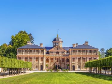 Schloss Favorite in Rastatt mit symmetrischer Barockfassade, zentraler Kuppel und gepflegten Gärten mit beschnittenen Bäumen entlang des Rasens.