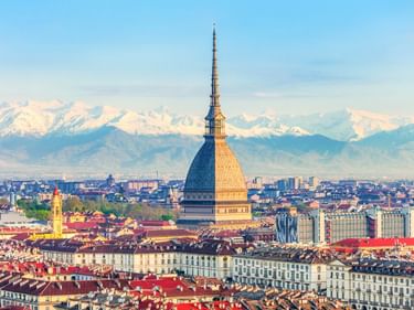 Panoramablick auf Turin mit dem ikonischen Turm Mole Antonelliana, der die Stadtlandschaft dominiert, schneebedeckte Alpen im Hintergrund.