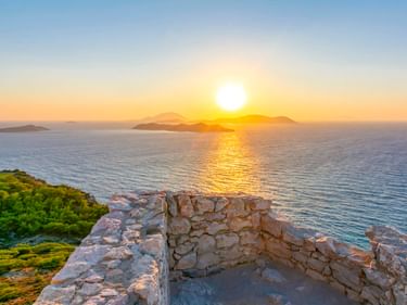 Antike Steinruinen in Kritinia mit Blick auf die Ägäis bei Sonnenuntergang, mit den Inseln Makri und Chalki am Horizont.