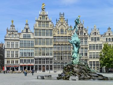 Brabo-Brunnen vor prächtigen Gildehäusern am Antwerpener Grote Markt. Bronzestatue zeigt eine Figur, die eine Hand wirft, umgeben von Wasser.