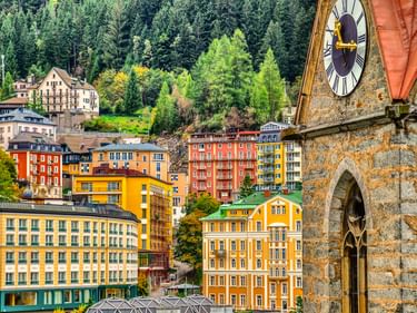 Bunte Gebäude in Bad Gastein mit historischem Kirchturm im Vordergrund und bewaldeten Bergen im Hintergrund.