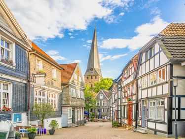 Kopfsteinpflasterstraße in Hattingens Altstadt, gesäumt von traditionellen Fachwerkhäusern. Ein hoher Kirchturm erhebt sich in der Mitte.