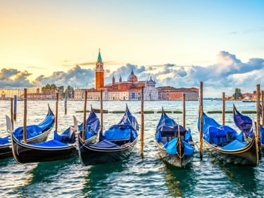 Blaue Gondeln an Holzpfählen in Venedig mit der Kirche San Giorgio Maggiore über dem Wasser unter dramatischem Abendhimmel.