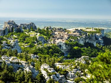 Les Baux-de-Provence auf felsigen Klippen mit Steingebäuden und Burgruinen, umgeben von grüner Vegetation und Ebenen.