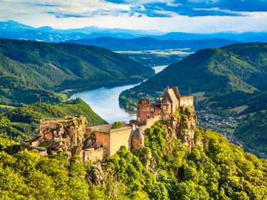 Burgruine Aggstein auf einem Felsen über der Donau, umgeben von bewaldeten Bergen und einem gewundenen Tal in Österreich.