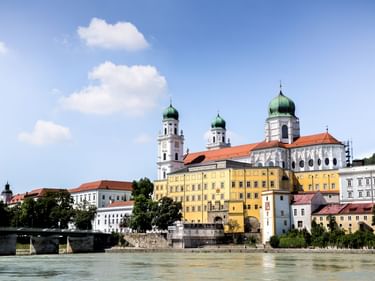 Blick auf Passaus Altstadt mit dem Stephansdom mit grünen Zwiebeltürmen und bunten historischen Gebäuden entlang der Donau.