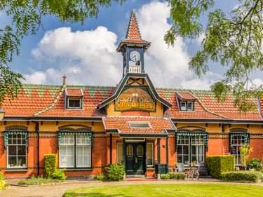 Historisches Gabbema Gasthuis-Gebäude in Leeuwarden mit roter Backsteinfassade, orangefarbenem Ziegeldach und Glockenturm. Grüner Rasen und Bäume rahmen den Eingang.