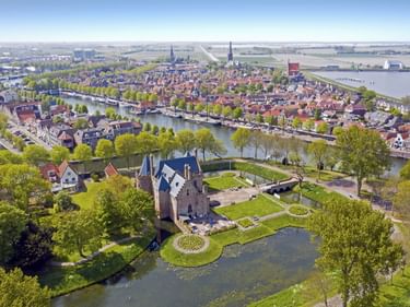 Luftaufnahme von Medemblik, Niederlande, mit mittelalterlichem Schloss umgeben von Wasser und Gärten, dahinter die historische Altstadt mit Grachten.