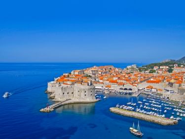 Luftaufnahme von Dubrovniks ummauerten Altstadt mit orangefarbenen Dächern, historischer Festung und Yachthafen im blauen Adriatischen Meer.