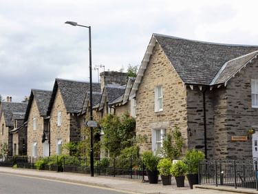 Reihe traditioneller schottischer Steinhäuser mit Schieferdächern in Pitlochry. Grüne Hecken säumen die Straße mit einer Laterne im Vordergrund.
