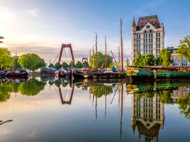Historische Schiffe im Alten Hafen von Rotterdam mit perfekten Spiegelungen im ruhigen Wasser. Das Witte Huis und die Willemsbrücke im Hintergrund.