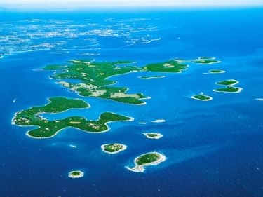 Luftaufnahme des Brijuni-Archipels in Kroatien mit grün bewaldeten Inseln, umgeben von hellblauem Wasser der Adria.