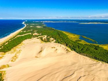 Luftaufnahme einer großen Sanddüne in Leba mit dichtem Wald, die die Ostseeküste von einer Lagune unter blauem Himmel trennt.