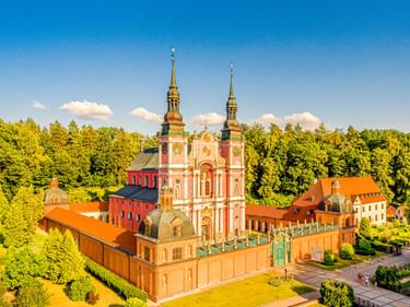 Luftaufnahme der barocken Basilika in Święta Lipka mit zwei Türmen, umgeben von Klostergebäuden und grünem Wald.
