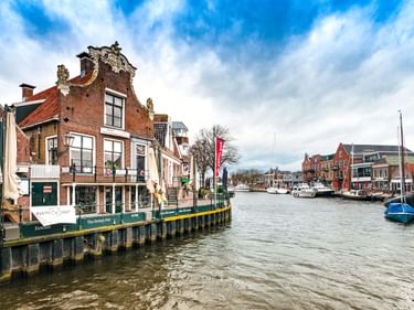 Kanalblick im Hafen von Lemmer mit traditionellen holländischen Backsteinhäusern, vertäuten Booten und bewölktem Himmel. Historisches Giebelhaus am Wasser.