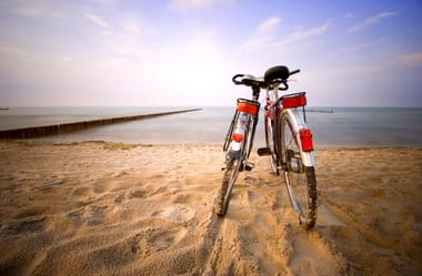 Bicycle with red panniers standing on sandy beach in Heringsdorf. Wooden pier extends into calm Baltic Sea under blue sky.