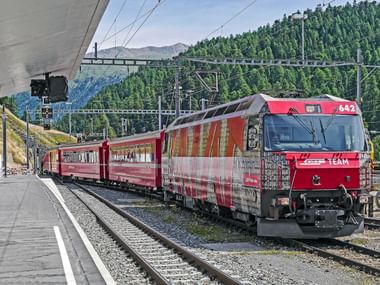 Roter Schweizer Zug am Bahnsteig in St. Moritz mit bewaldeten Bergen im Hintergrund. Die Lokomotive zeigt die Nummer 642.
