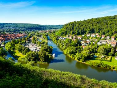 Luftaufnahme von Hann. Münden, wo Werra und Fulda zusammenfließen, umgeben von bewaldeten Hügeln und historischer Stadt mit roten Dächern.