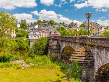 Alte Steinbrücke mit verzierter Laterne über einem Fluss in Weilburg, mit historischen Gebäuden und grünen Bäumen im Hintergrund.
