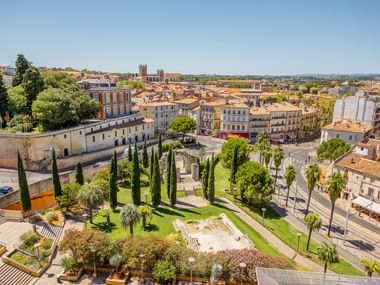 Panoramablick auf Montpellier mit historischen Gebäuden, einem grünen Park mit Zypressen im Vordergrund und der Kathedrale in der Ferne.