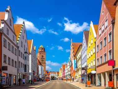 Straßenansicht in Donauwörth Altstadt mit bunten historischen Gebäuden und einem Turm unter blauem Himmel. Orangefarbene Dächer säumen die Fußgängerzone.