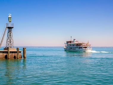 Weiße Personenfähre fährt auf türkisfarbenem Bodensee-Wasser nahe Rorschach Hafen mit Navigationsturm und Holzpier im Vordergrund.