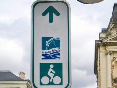 Wegweiser für Loire à Vélo Radweg mit Pfeil nach oben, Routenlogo mit Wellendesign und Radfahrersymbol an Mast in städtischer Umgebung.