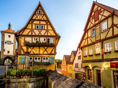 Historische Fachwerkhäuser am Plönlein in Rothenburg ob der Tauber mit Brunnen, Torturm und Kopfsteinpflaster unter blauem Himmel.