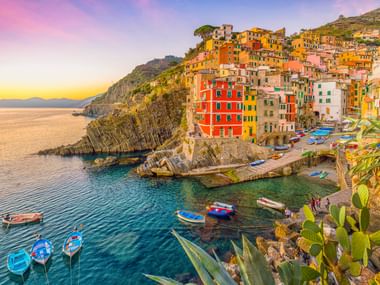 Bunte Häuser von Riomaggiore in Cinque Terre auf Felsen über einem kleinen Hafen mit Fischerbooten bei Sonnenuntergang.