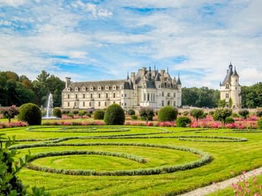 Château de Chenonceau mit Renaissance-Architektur, formalen Gärten mit kreisförmigen Mustern, rosa Blumen und einem Brunnen.
