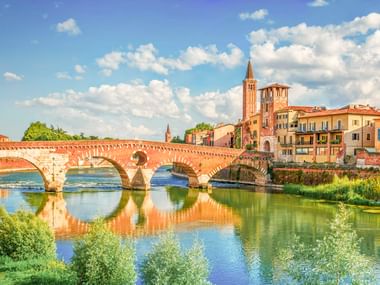 Antike römische Steinbrücke Ponte Pietra mit fünf Bögen über die Etsch in Verona, mit historischen Gebäuden und Kirchturm.