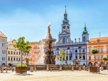 Historischer Marktplatz in Budweis mit Samson-Brunnen und barockem Rathaus mit Uhrturm, umgeben von bunten Gebäuden.