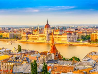 Panoramablick auf Budapest mit dem ungarischen Parlamentsgebäude an der Donau. Historische Dächer im Vordergrund, Stadtbild im Hintergrund.