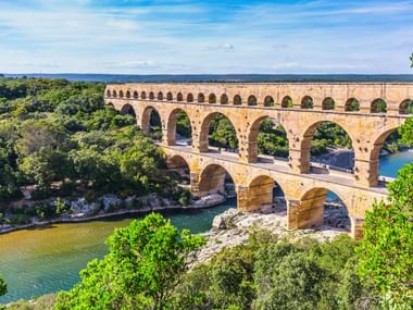 Pont du Gard, antikes römisches dreistöckiges Aquädukt aus Stein über dem Gardon, umgeben von grünen Bäumen unter blauem Himmel.