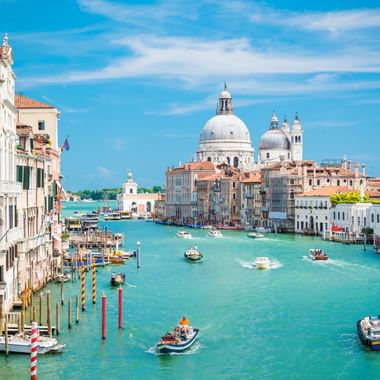 Venedigs Canal Grande mit türkisfarbenem Wasser, Booten, bunten Gebäuden und der ikonischen Kuppel der Basilika Santa Maria della Salute.