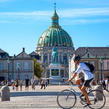 Radfahrerin fährt an der Frederikskirche mit ihrer markanten türkisfarbenen Kuppel in Kopenhagen vorbei. Fußgänger auf dem Platz.