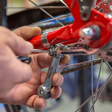 Close-up of hands using a tool to adjust the rear derailleur on a bicycle with red frame and disc brake.