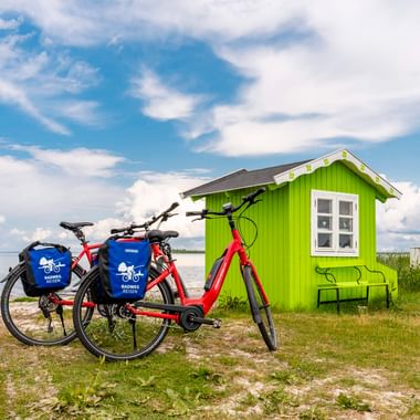 Zwei Fahrräder mit blauen Taschen neben einem leuchtend grünen Strandhaus mit weißen Fenstern in Ærøskøbing, Dänemark. Meer und blauer Himmel.
