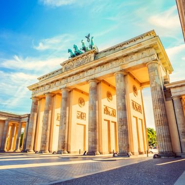 Brandenburger Tor in Berlin mit neoklassizistischen Säulen und Quadriga-Skulptur, beleuchtet von warmem Sonnenlicht unter blauem Himmel.
