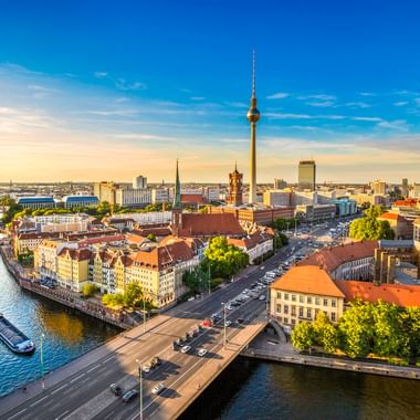 Luftaufnahme von Berlin mit Fernsehturm, Spree und historischen Gebäuden unter blauem Himmel. Ein Boot fährt auf dem Fluss.