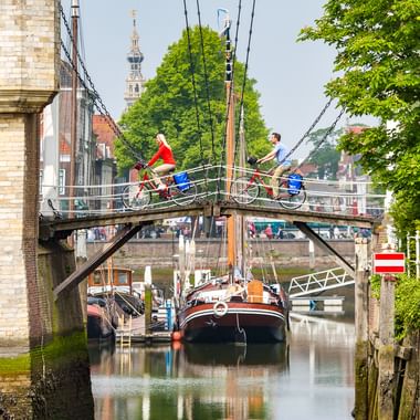 Zwei Radfahrer überqueren eine Zugbrücke über einen Kanal in Zierikzee, Niederlande. Ein Boot liegt darunter, im Hintergrund ein Kirchturm.