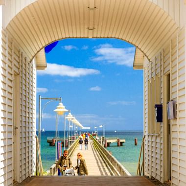 Blick durch den Bogeneingang des Seebrückengebäudes Ostseebad Göhren. Weiße Holzkonstruktion rahmt die Seebrücke ein, die mit Laternen in die Ostsee führt.