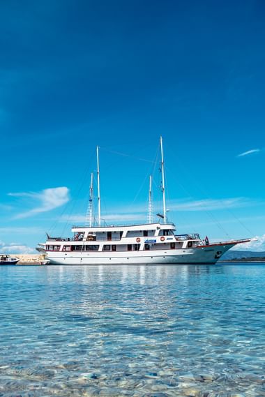 Weiße Motoryacht mit zwei Masten ankert in klarem türkisfarbenem Wasser nahe der kroatischen Küste unter blauem Himmel.