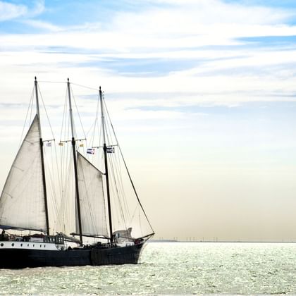 Traditionelles Segelschiff Mare fan Fryslan mit dunklem Rumpf und drei weißen Segeln auf ruhigem Wasser unter bewölktem Himmel.