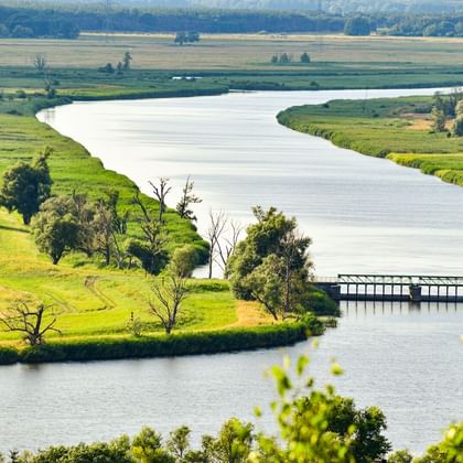 Aerial view of the Oder River winding through green meadows near Widuchowa. A small bridge crosses the river, with trees lining the banks.